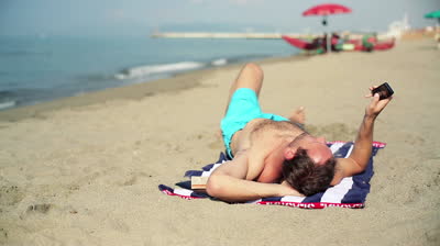 stock-footage-young-man-using-smartphone-on-the-beach